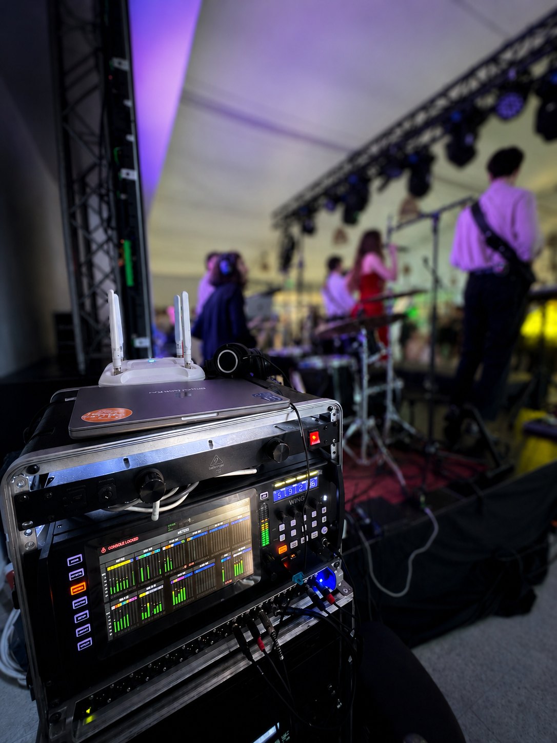 Stage rack with a digital mixer next to a band playing live